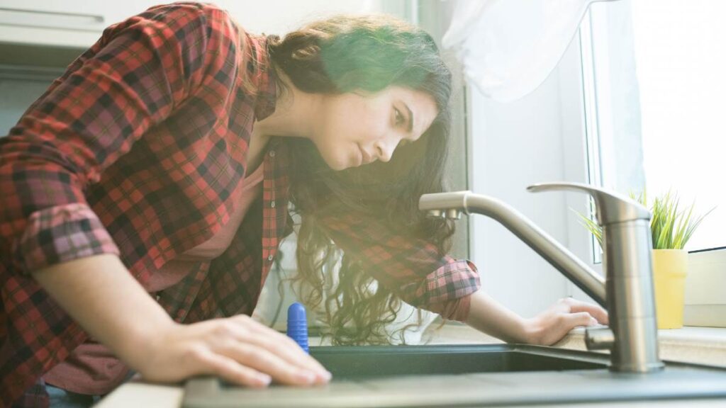 Woman leaning over and inspecting a kitchen faucet.