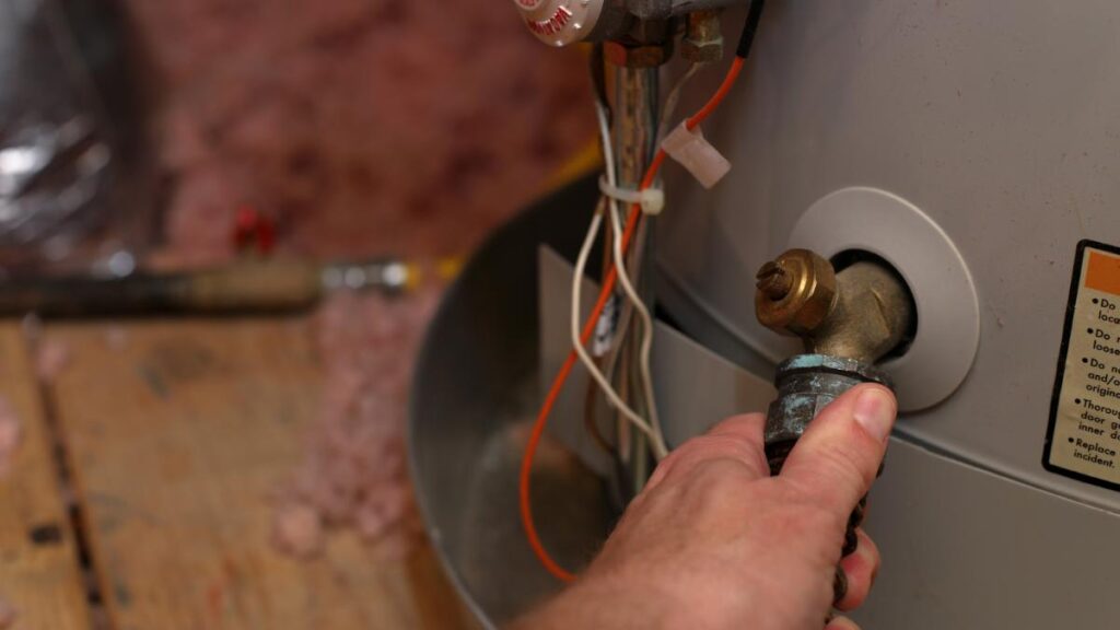 Close up of a hand attaching a hose to a hot water tank.