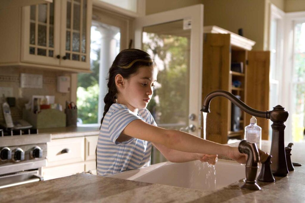 Young girl washing her hands in a kitchen sink.