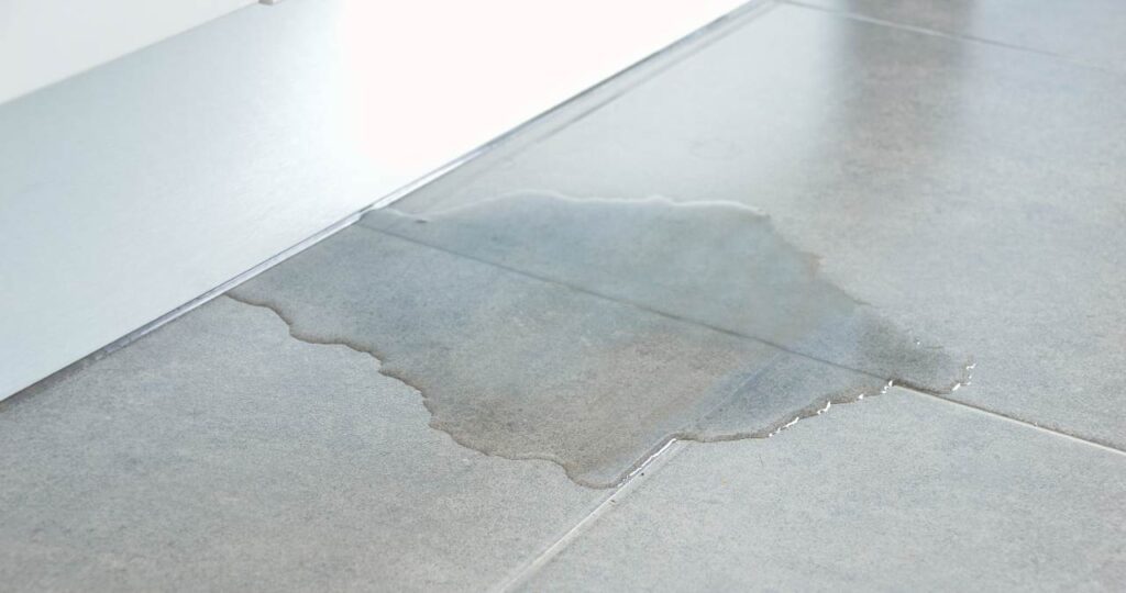 Water pooling underneath a door onto a grey tile floor.