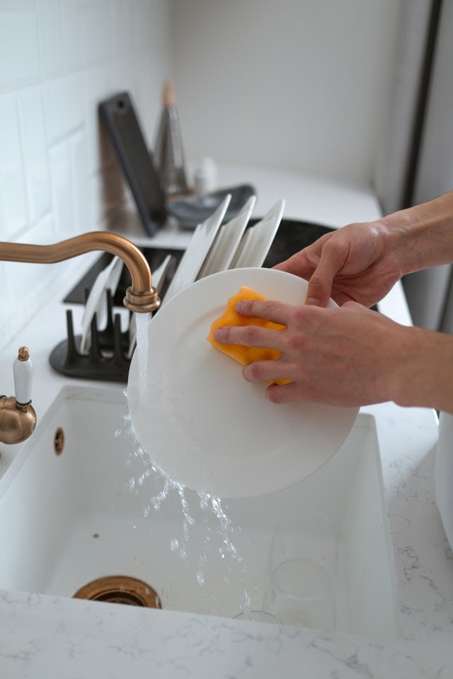 Hands washing a dish in a white kitchen sink.