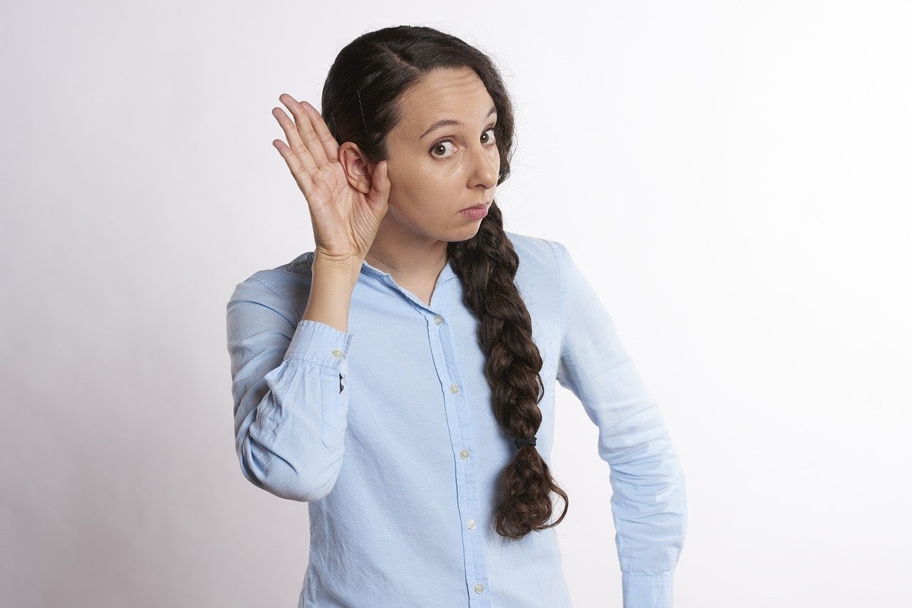 Woman with a confused expression holding a hand up to her ear.