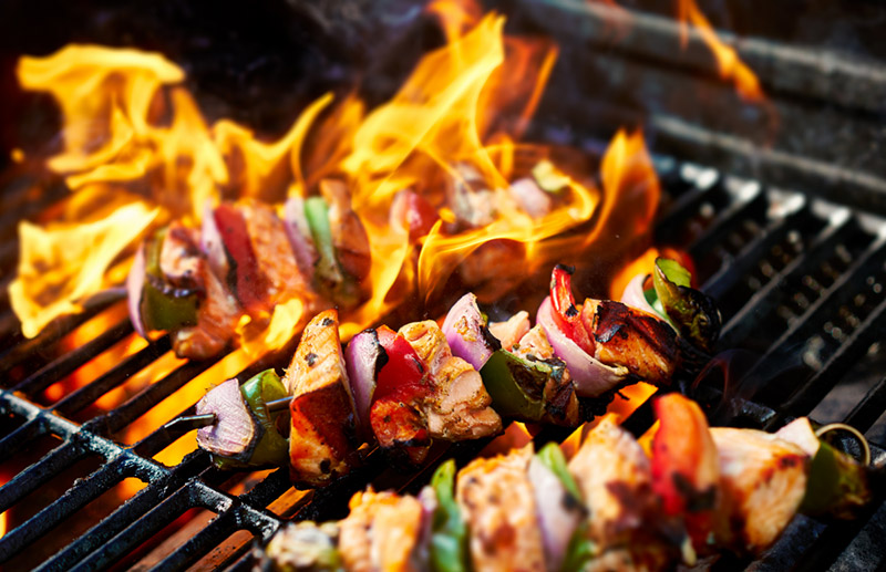 Chicken kebabs cooking on a flaming grill.