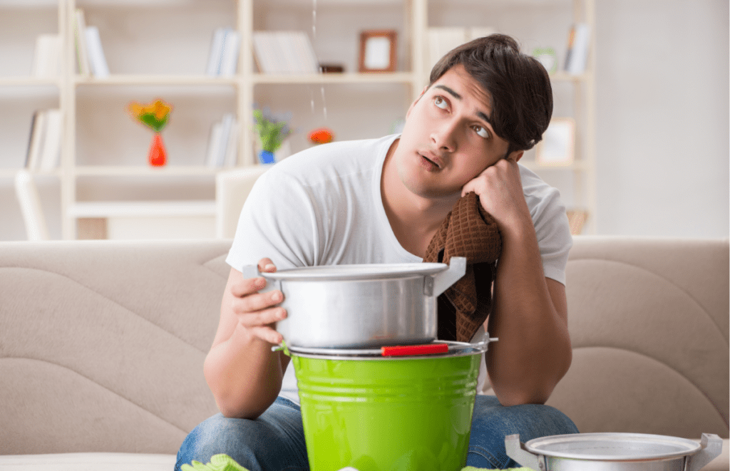 Man sitting on a couch holding a bucket under a leak.